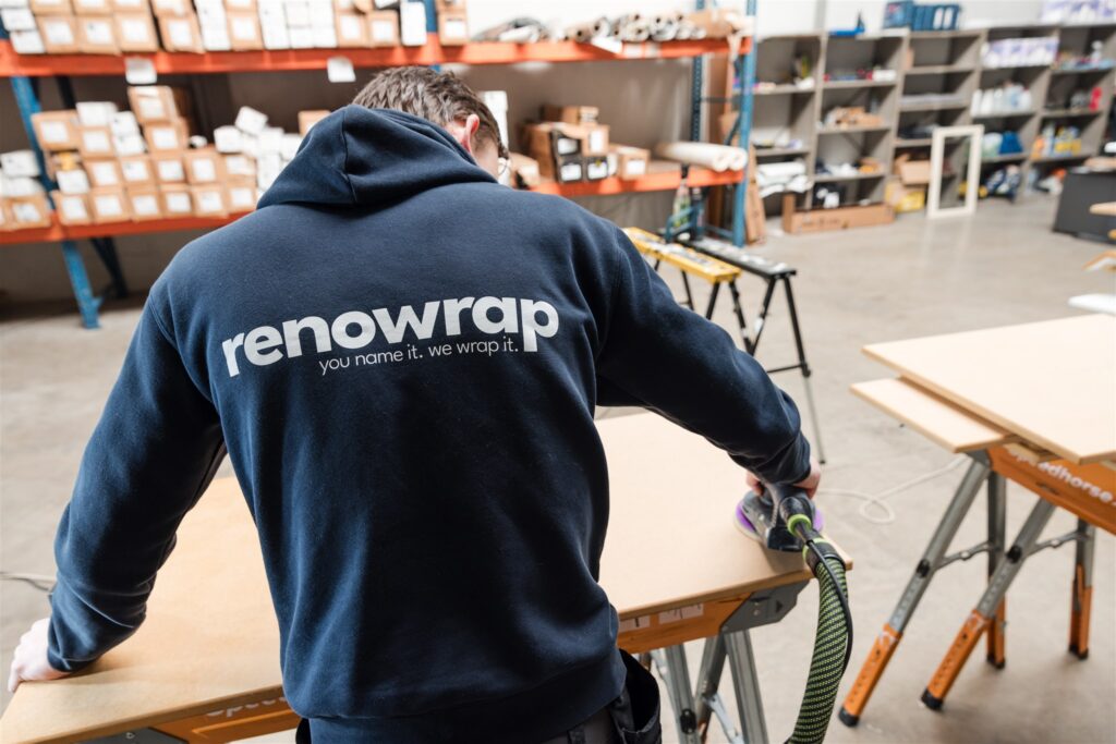 medewerker renowrap schuurt houten oppervlak in werkplaats met materialen op achtergrond